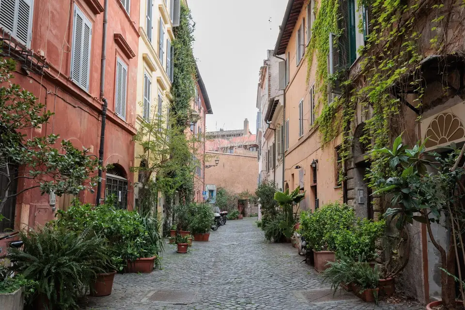 The cobbled Trastevere lane, ochre and red façades, potted plants at the doorways.